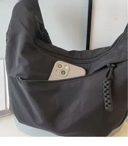 Detail of moon-shaped nylon bag showing the front zipper pocket with phone for scale