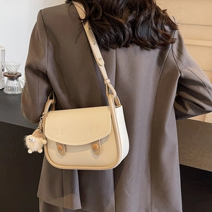 Elegant off-white saddle shoulder bag with brown trim and plush charm worn by a model