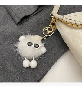 Close-up of white plush ball keychain with sunglasses hanging on a woven handbag strap