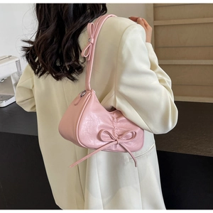 Detail of pink pleated underarm bag with decorative bow and textured PU leather