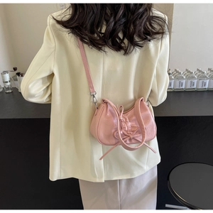 Detail of pink pleated crossbody bag featuring a bow, shown on a model for scale