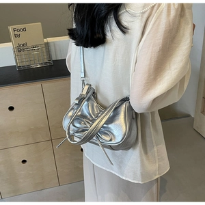 Silver metallic pleated crescent bag with bow detail worn by a model in a natural setting