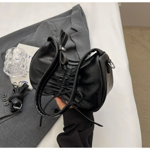 Detail of black pleated underarm bag with decorative leather bows and oil wax finish