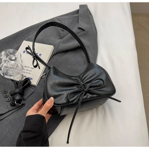 Detail of black pleated bow shoulder bag with detachable strap on a minimalist background
