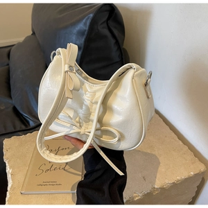Close-up of cream-colored pleated hobo bag with bow details and textured PU leather finish