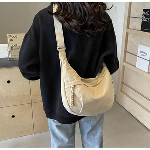 Detail of a beige nylon crescent bag with woven zipper pull and adjustable wide strap