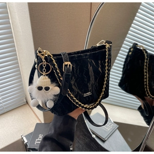 Detail of black pleated bucket bag with gold chain and plush doll pendant