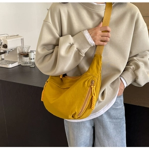 Detail of yellow nylon crescent crossbody bag worn by a model in a cafe setting