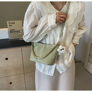 Detail of light green bucket bag with gold chain strap and plush ball charm on a model