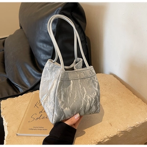Detail of silver metallic tote bag with pleated texture on a stone surface