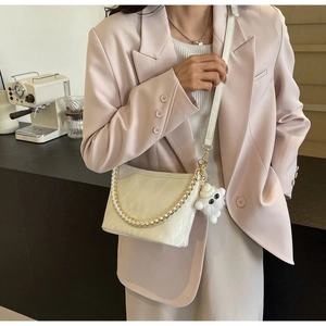 Detail of a creamy beige chain bucket bag featuring a soft faux fur pompom and gold chain