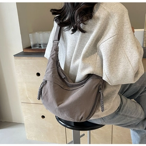 Neutral grey nylon crossbody bag shown worn by a model in a minimalist home setting