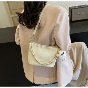 Detail of beige bucket bag with pleated PU texture, golden chain and plush bear charm