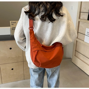 Detail of vibrant orange nylon crescent crossbody bag worn by a model in a casual setting