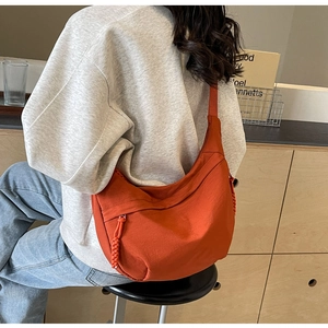 Detailed view of bright orange nylon crossbody bag worn by model in a cozy setting