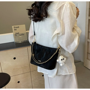 Detail of black chain bucket bag with plush monster charm worn by a model in a warm room