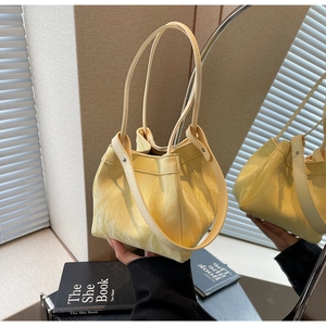 Close-up of hand holding a light yellow glossy leather bucket bag with pleated texture