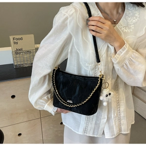 Detail of black pleated shoulder bag with gold chain and white eye-shaped pompom charm