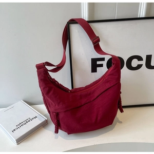 Detail of burgundy crescent shoulder bag with woven zipper pull and adjustable strap