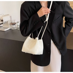 Detail of off-white bucket bag with pleated texture and metal studs on café table