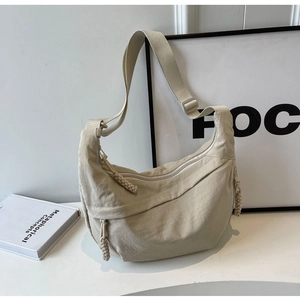 Close-up of beige nylon crescent bag featuring ruched fabric and braided rope zipper pulls