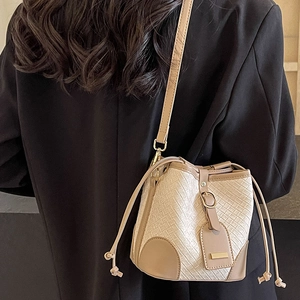 Minimalist woven bucket bag with brown leather trim and drawstring closure on shoulder