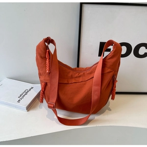 Detail of orange crescent bag with textured fabric and woven ball zipper pull