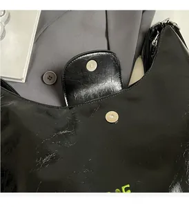 Dettaglio della borsa tote in pelle verniciata nera con ricami verdi e chiusura magnetica