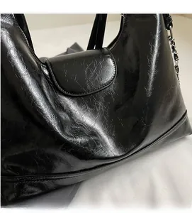 Dettaglio borsa in pelle verniciata nera con ricamo verde e tracolla a catena
