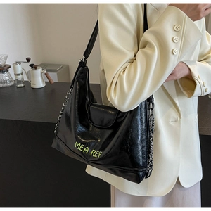 Dettaglio borsa tote nera lucida con scritta MEA REY verde neon e catena d'argento