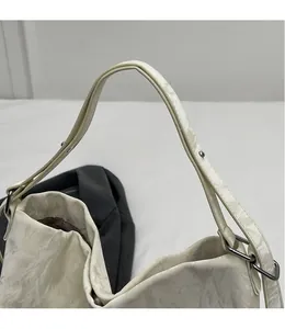 Detail of smooth shoulder strap and metal ring hardware on pleated beige tote bag