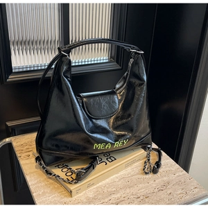 Dettaglio della borsa nera lucida con logo verde neon e tracolla con catena metallica