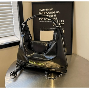 Dettaglio della borsa tote in pelle verniciata nera con logo verde neon e catena argento