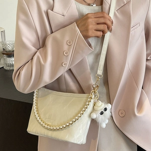 Elegant cream bucket bag with woven chain and plush pendant worn on a pink blazer