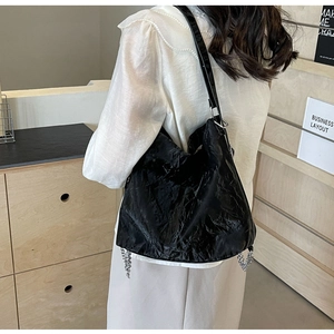 Detail of black tote bag with wrinkled texture and silver chain on model back