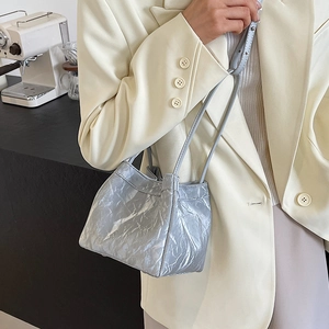 Silver wrinkled texture mini bucket bag shown on shoulder of a model in beige suit
