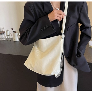 Detail of cream pleated tote bag with silver chain worn by model in black blazer