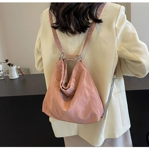 Model wearing a light pink wrinkled tote bag with silver chain details and adjustable strap