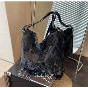Detail of black wrinkled texture tote bag with silver chain and wide shoulder strap