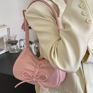 Pink crescent underarm bag featuring delicate pleats and bow accents on a leather finish