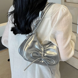 Silver metallic pleated underarm bag with bow detail worn by a model in soft lighting