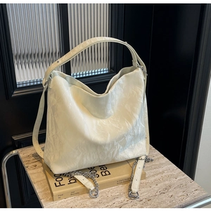 Detail of cream white pleated hobo bag with silver chain on marble surface