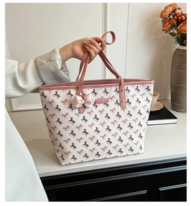 Detail of a large tote bag with pink handles, horse print, and a silk bow accessory