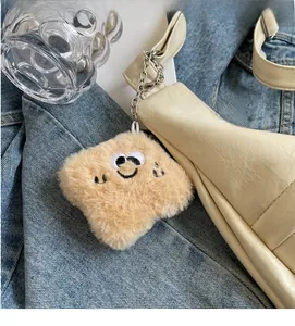 Detail of a plush smiley face bag charm with golden metal chain on a leather handbag