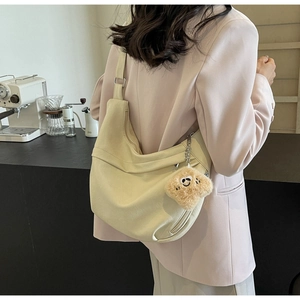Detail of off-white hobo bag with adjustable strap and plush smiley charm in a cafe setting