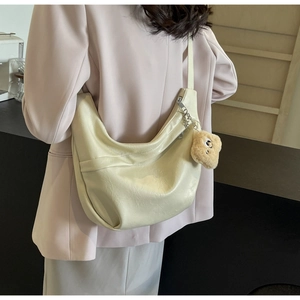 Detail view of large cream hobo bag with cute bear charm worn over a pink blazer