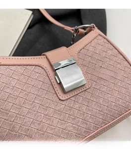 Close-up of pink woven underarm bag featuring a silver metal lock and leather trim