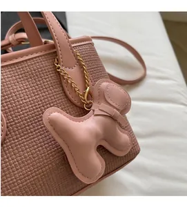 Dettaglio della borsa intrecciata rosa con scritte dorate e ciondolo a forma di cane