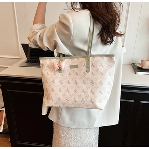 Detail of cream tote bag with horse print and green handles worn in office setting