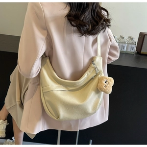 Detail of a beige crescent crossbody bag with a cute brown plush bear charm and soft PU leather